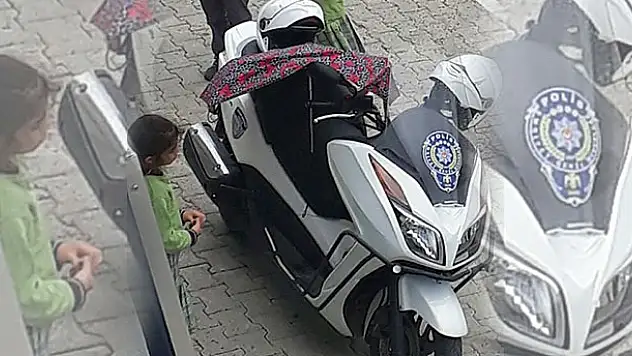 Polisin motosikleti ıslanmasın diye şemsiyeyle bekleyen küçük kız.